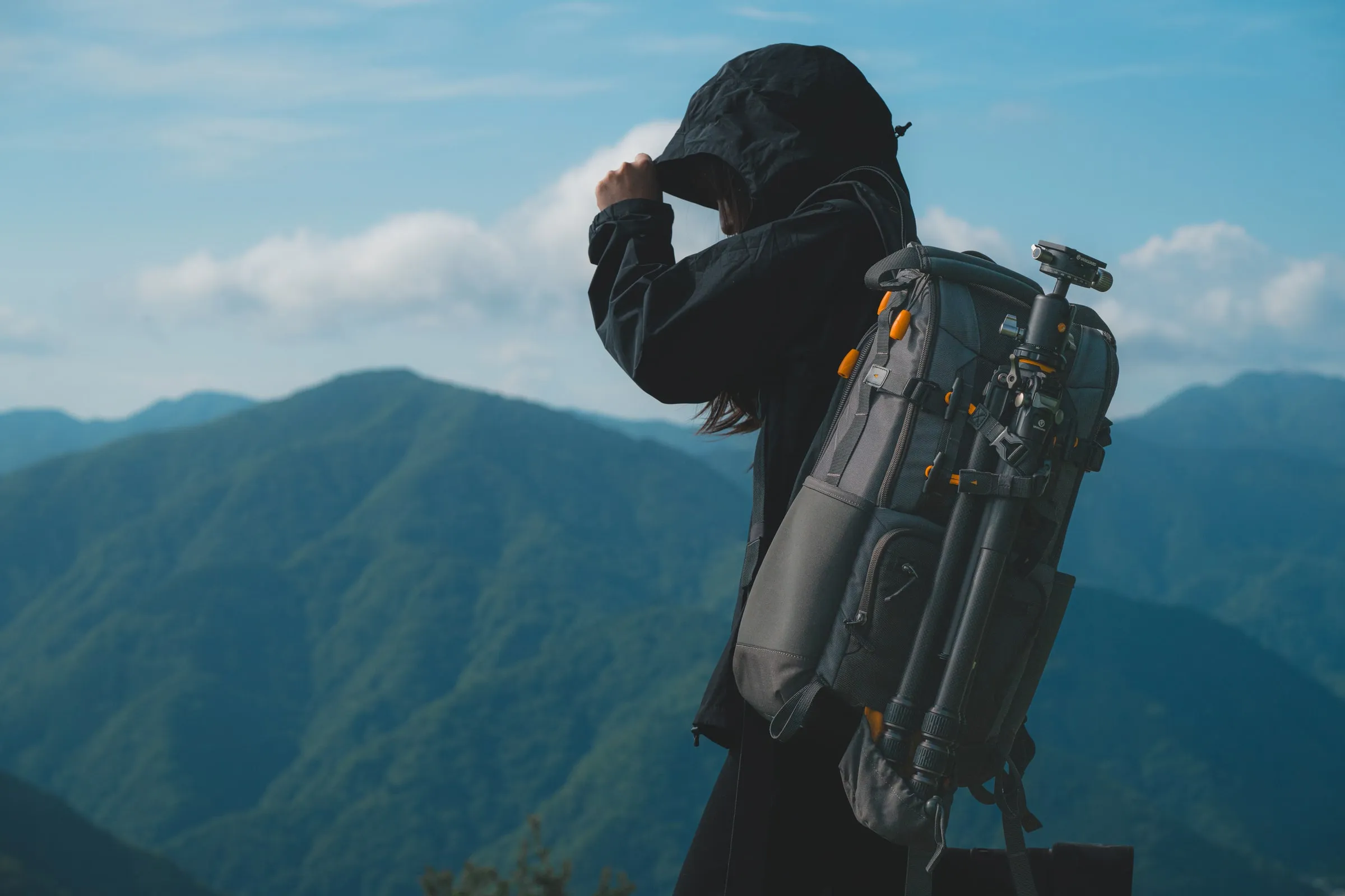 山を背景にカメラバッグを背負ったモデル